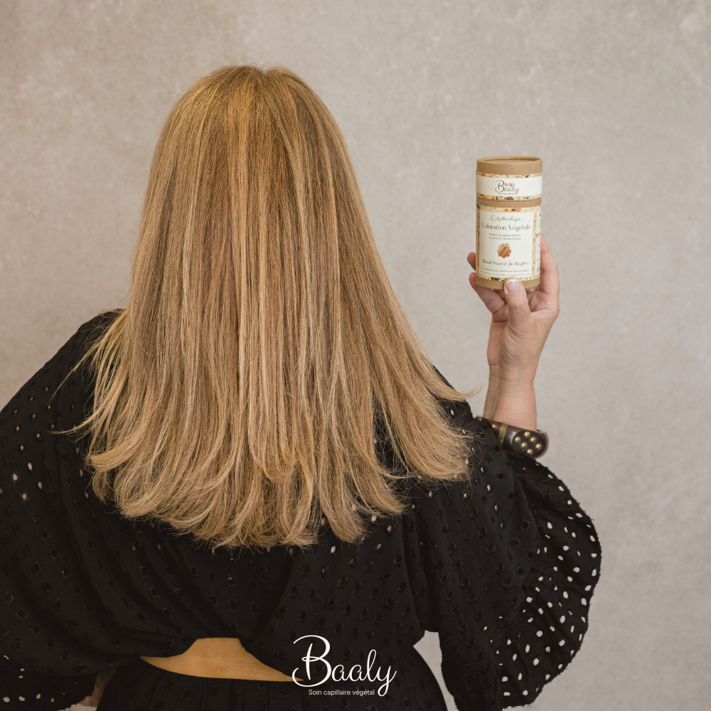 Femme blonde avec coloration végétale personnalisée Baaly, tenant son pot de poudre après diagnostic capillaire. Résultat blond naturel avec le blond de Brigitte, lumineux et adapté à chaque cheveu.